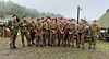 Military reenactors in brown uniforms and red berets stand at an outdoor camp