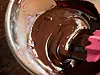 Melted dark chocolate being stirred in a glass mixing bowl with a pink spatula.