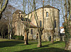 Stone church with a tower in a grassy area among bare trees.
