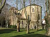 Stone church with a tower in a grassy area among bare trees.