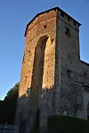 Sunlit historic stone tower made of weathered brick against a blue sky.