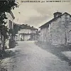 Black and white image of a quiet village street lined with stone buildings and a small chapel in the distance.