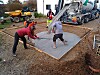 Construction workers spreading wet concrete beside a cement mixer and dump truck.