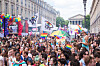 Large crowd dancing in Paris with rainbow flags and a decorated float in the background.