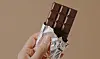 A hand holding a partially unwrapped dark chocolate bar