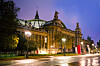 The Grand Palais in Paris lit up at night beside a wet, reflective street.