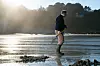 Person standing in shallow water on a muddy tidal flat at sunrise.