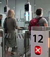Two travellers with luggage pass through an airport security Parafe gate marked 12.