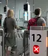 Two travellers with luggage pass through an airport security Parafe gate marked 12.