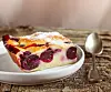 Slice of clafoutis cherry pie on a grey plate with a spoon beside it.