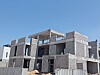 Partially built villa with concrete block walls and open window spaces behind a site fence.