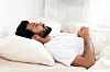Indian man lying in bed, awake and looking distressed, with white pillows and bedding.