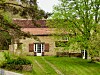 Converted French barn with tiled roof, shutters and grassy garden under leafy trees.