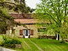 Converted French barn with tiled roof, shutters and grassy garden under leafy trees.