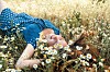 Blonde woman lying in a chamomile field wearing a blue polka-dot dress.