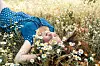 Blonde woman lying in a chamomile field wearing a blue polka-dot dress.