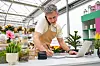 Shop owner writing an order at a counter in a plant shop with a laptop and potted plants.