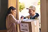 Delivery worker and recipient signing paperwork beside a parcel at the door.