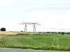 Transmission towers and power lines over green farmland beneath a pale sky.
