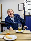 Smiling man seated at a table in Bistrot Bertha with a glass of beer in front of him.