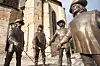 Bronze statues of D'Artagnan and other figures in front of a stone building in Condom, France.