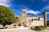 Stone gate and medieval walls of Larressingle in Gers, Occitanie, beneath a blue sky.