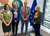 Four people standing indoors beside a European Union flag in a bright office.