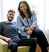 Two smiling colleagues seated on a sofa in a bright office.