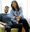 Two smiling colleagues seated on a sofa in a bright office.