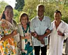 Four people standing together and smiling outdoors in a leafy garden area.