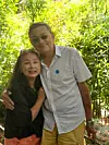 A couple poses together in front of dense green plants in a garden.