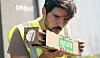 Man in a reflective vest looking closely at a cardboard package with printed branding.