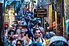 Crowded narrow street in Mont-Saint-Michel with tourists, shops and a Creperie Du Chapeau Rouge sign.