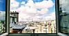 Open window framing rooftops and a distant city skyline under clouds.
