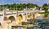 Stone arch bridge over the Loire River in Tours, France, with buildings and trees in the background.