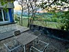 Metal table and chairs on a stone terrace beside a building, overlooking a green valley at sunset.