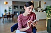 Young Latina woman sitting in a living room and using a smartphone.