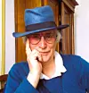 Man in a blue hat and glasses posing indoors, resting his chin on his hand.