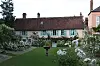 Traditional brick house beside a formal garden with a lawn, white flowers and shrubs.