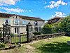 Stone gate in front of a traditional house with a garden and blue sky.