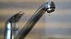 Close-up of a chrome kitchen faucet with a single drop of water falling.