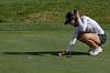 Golfer crouches on the green, marking a ball and lining up a putt.