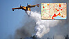 A firefighting plane drops water on a wildfire with heavy smoke rising.