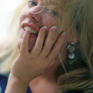 Close-up of a blonde woman smiling with her hand on her cheek.