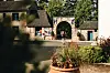 Person standing by a stone archway on a village street, with cottages and a flower planter.