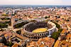 Aerial view of Nîmes historic centre with a Roman amphitheatre and surrounding red-roofed buildings.