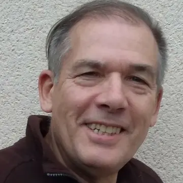 Close-up of a smiling middle-aged man against a textured wall.