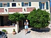 Woman standing outside a building beside trees and a gravel driveway.