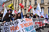 Crowd of protesters holding banners and flags during a march on a city street.