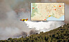 Helicopter drops water on a smoky wildfire over a forested mountainside.